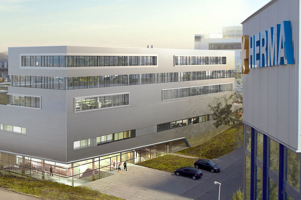 Moderne Bürogebäude mit flacher Dachlandschaft und großen Fenstern, umgeben von einer grünen Fläche und einem Parkplatz.